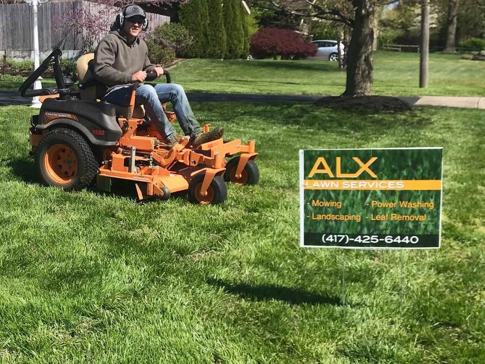 ALX crew member mowing a lawn on a zero-turn mower behind an ALX yard sign
