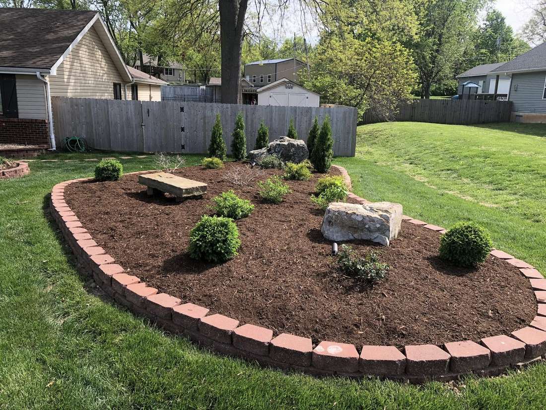 Finished landscape bed with brick edging, fresh mulch, boulders, boxwoods and young arborvitae